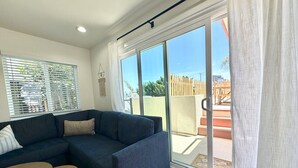 A modern living room with a sectional sofa, a small round table, and a sliding glass door leading to an outdoor area. - NEW July 2026 Remodel! Triton`s Castle Overlooking Beach and Bay! (San Diego)