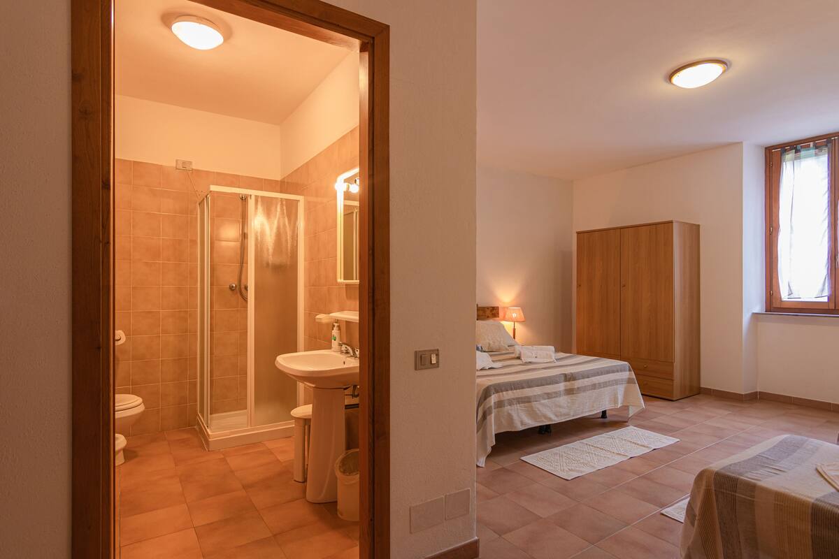 A bedroom with a bed, a nightstand, a wooden wardrobe, and a window with curtains.