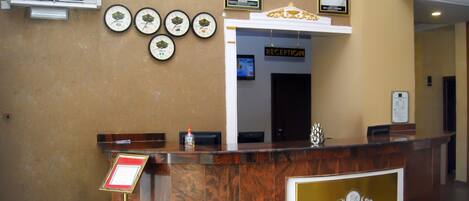 A reception desk with a GLO-RAN Hotel and Event Place sign, multiple clocks, and framed portraits above the desk.