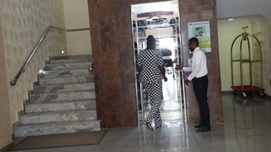 A marble staircase with a handrail, a digital elevator display, and a poster on the wall. - Glo-ran Hotel and Event Place (Owerri)