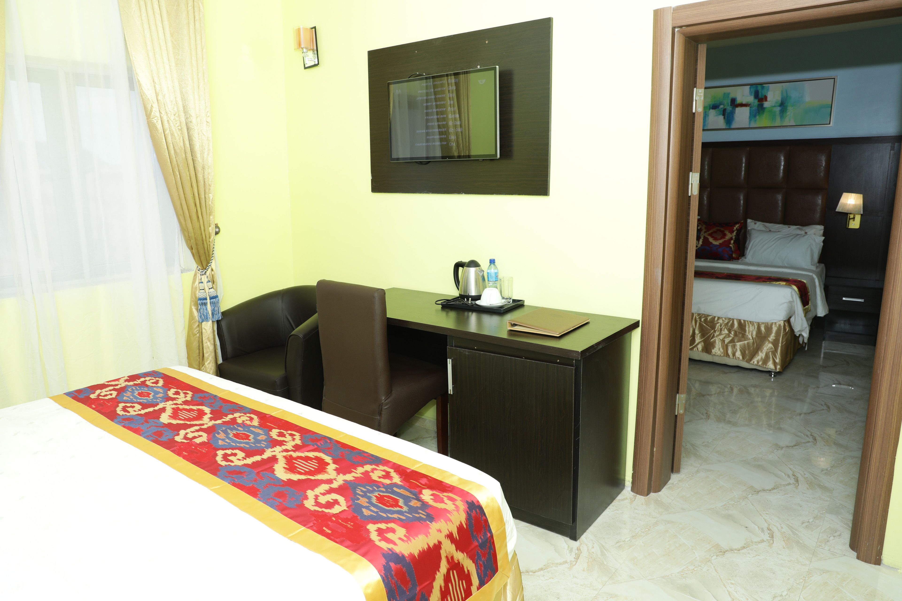 A hotel room with a bed, desk, chair, and a television on the wall.