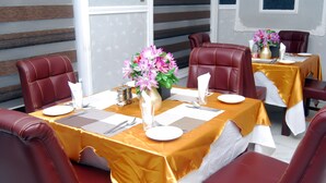 A dining area with tables set for four, each with a vase of flowers, white tablecloths, and red leather chairs. - Glo-ran Hotel and Event Place (Owerri)