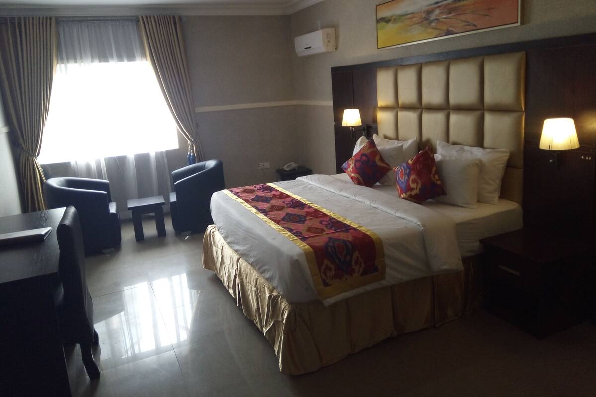 A hotel room with a bed, bedside lamps, a desk, and a chair.