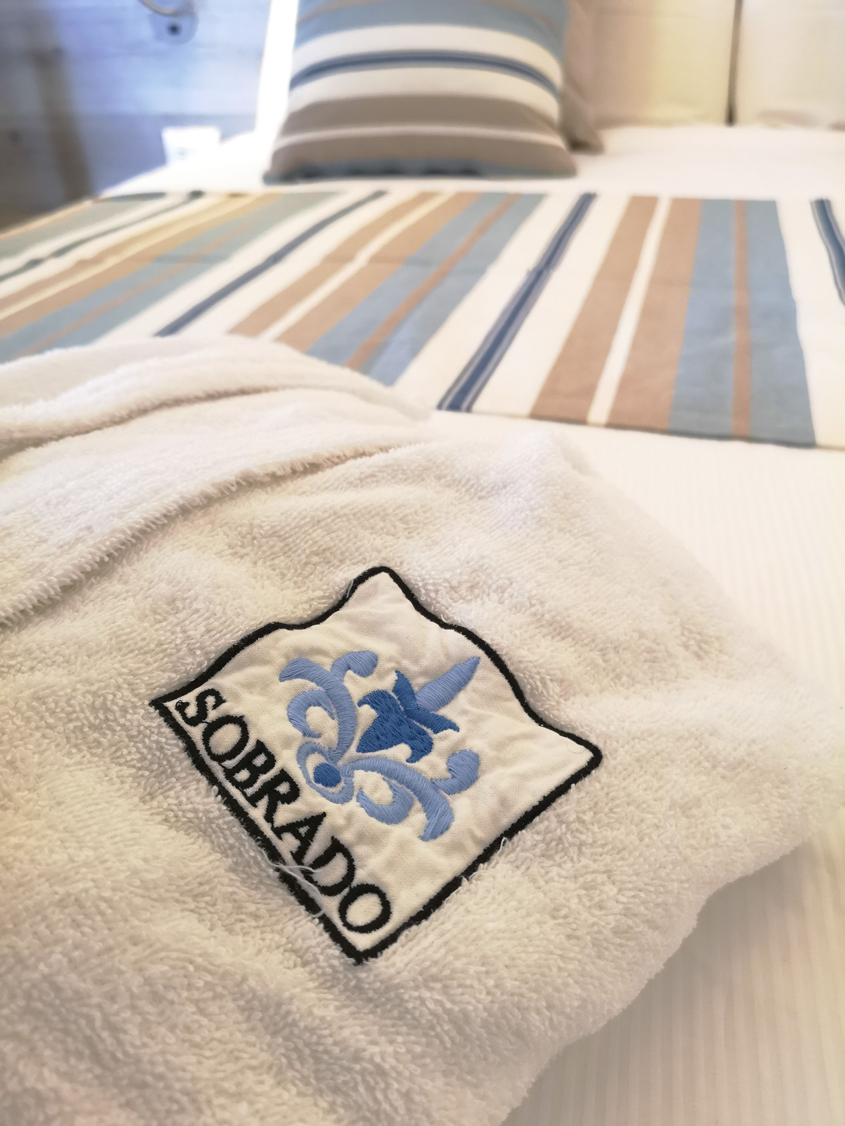 Ein Bett mit gestreifter Bettwäsche und ein Handtuch mit aufgestickter Schrift.