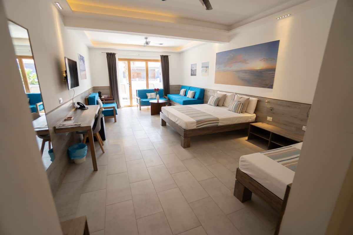 A modern hotel room with a large bed, a desk, a sofa, and a view of the outdoors.