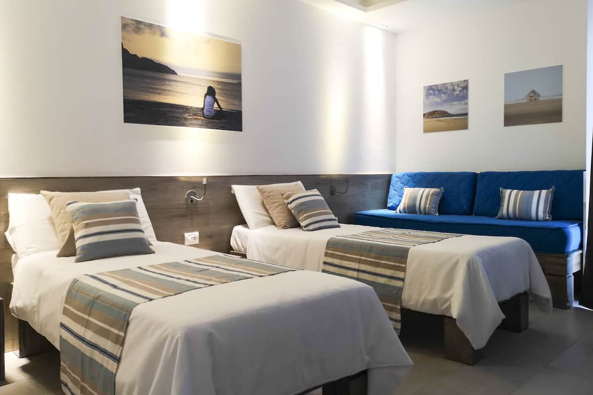 A hotel room with two beds, a blue sofa, and wall art depicting landscapes.