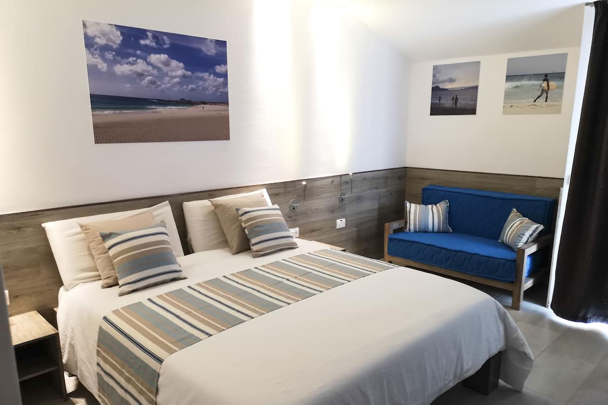 A bedroom with a bed, a blue sofa, and wall art depicting beach scenes.