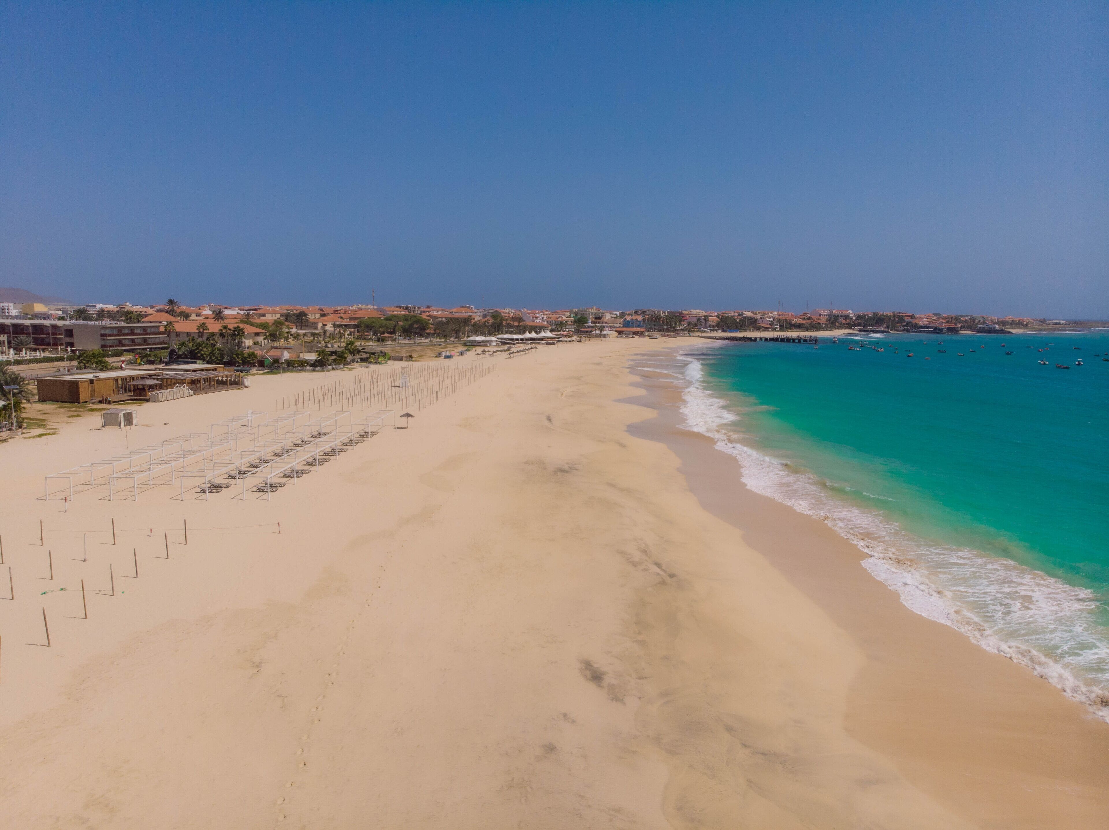 A beach with clear turquoise waters, a sandy shore, and a row of beach umbrellas.