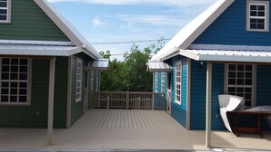 Une terrasse en bois reliant deux maisons dont les murs sont recouverts de bardage vert et bleu.