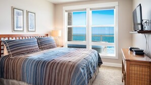Un dormitorio con cama, televisor, lámpara y ventana con vista al mar.