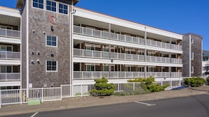 Un hotel de varios pisos con balcones, un letrero que dice 'Pacific Winds' y un cielo azul despejado.