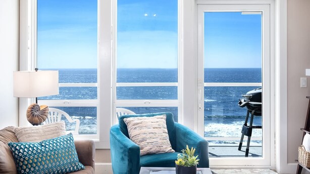 Una sala de estar con un ventanal grande, un sillón color turquesa, una mesa de centro y una lámpara.