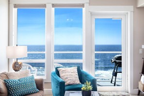 A living room with a large window, a teal armchair, a coffee table, and a lamp. - Pacific Rim Retreat with Fireplace & Hot Tub (Lincoln City)