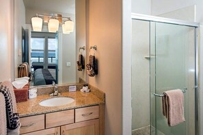 Une salle de bain avec un lavabo sur un plan de travail en granit, un miroir et une cabine de douche en verre.