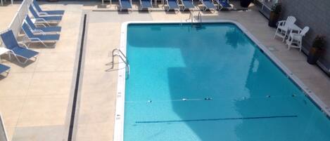 A rectangular swimming pool with blue water, surrounded by lounge chairs and a stone wall.
