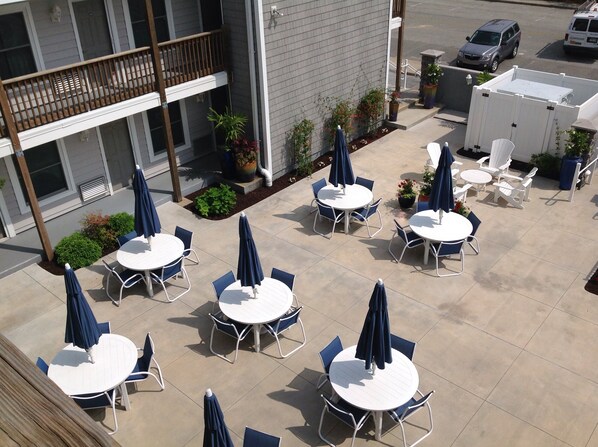An outdoor patio area with multiple round tables and chairs, some with blue umbrellas. - Stroll to North Ocean City Beaches, cozy 1-bedroom condo awaits (Ocean City)
