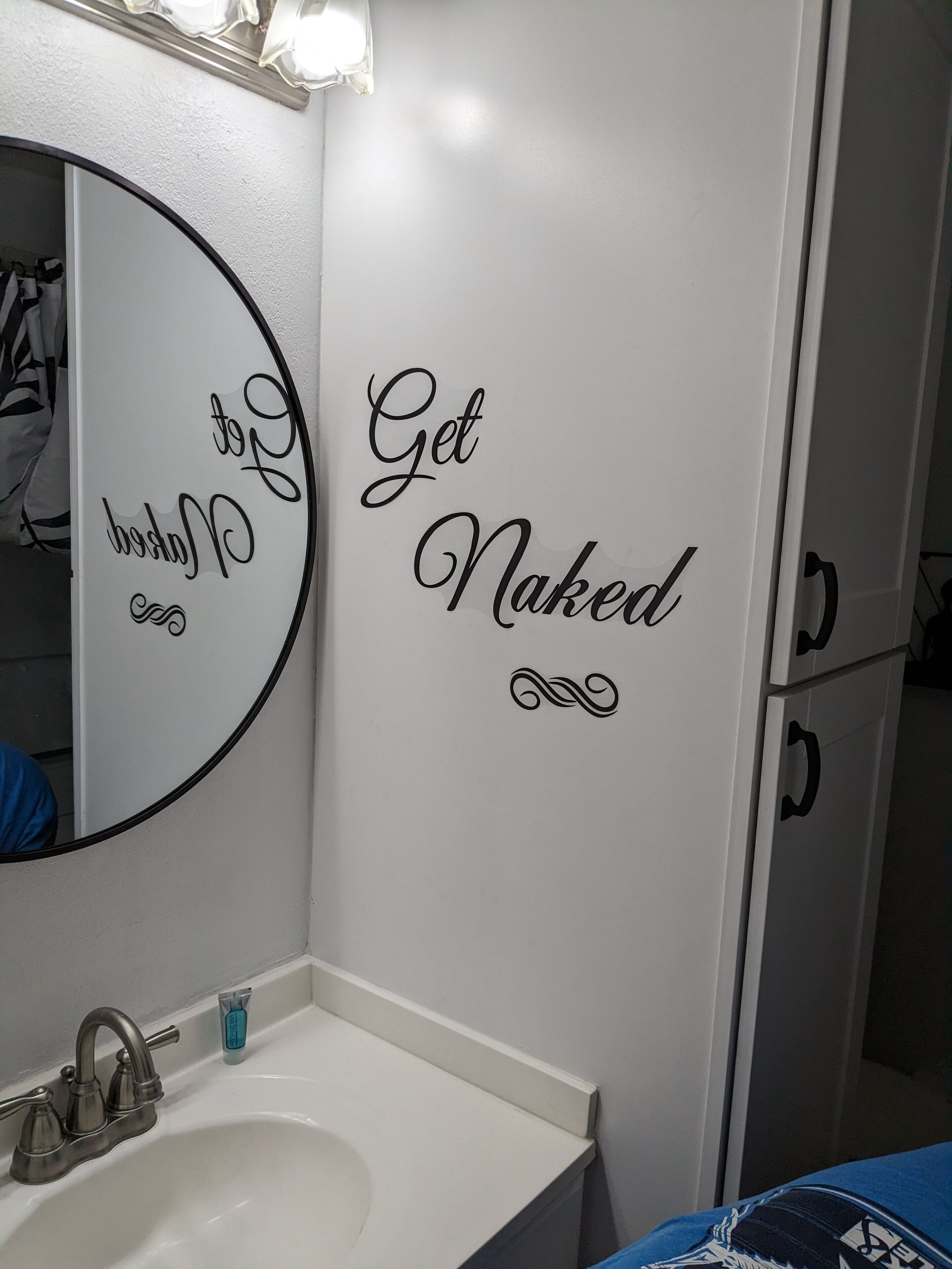 A bathroom with a white sink, a mirror, and a wall with the text "Get Naked".