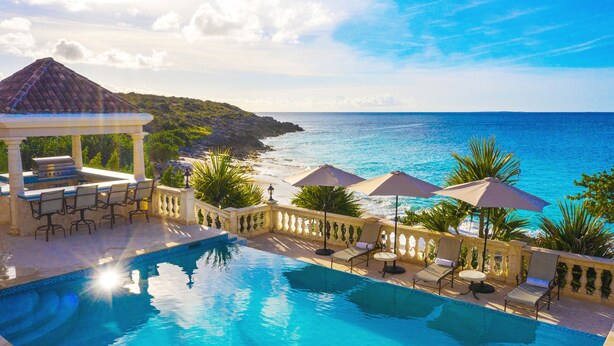 A pool area with a gazebo, lounge chairs, and umbrellas overlooking a beach and ocean.