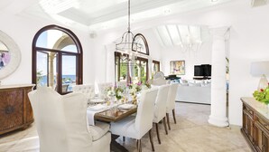 A spacious dining area with a high ceiling, large windows, and a view of the sea.