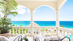 A balcony with white columns, a view of the ocean, and a potted plant.