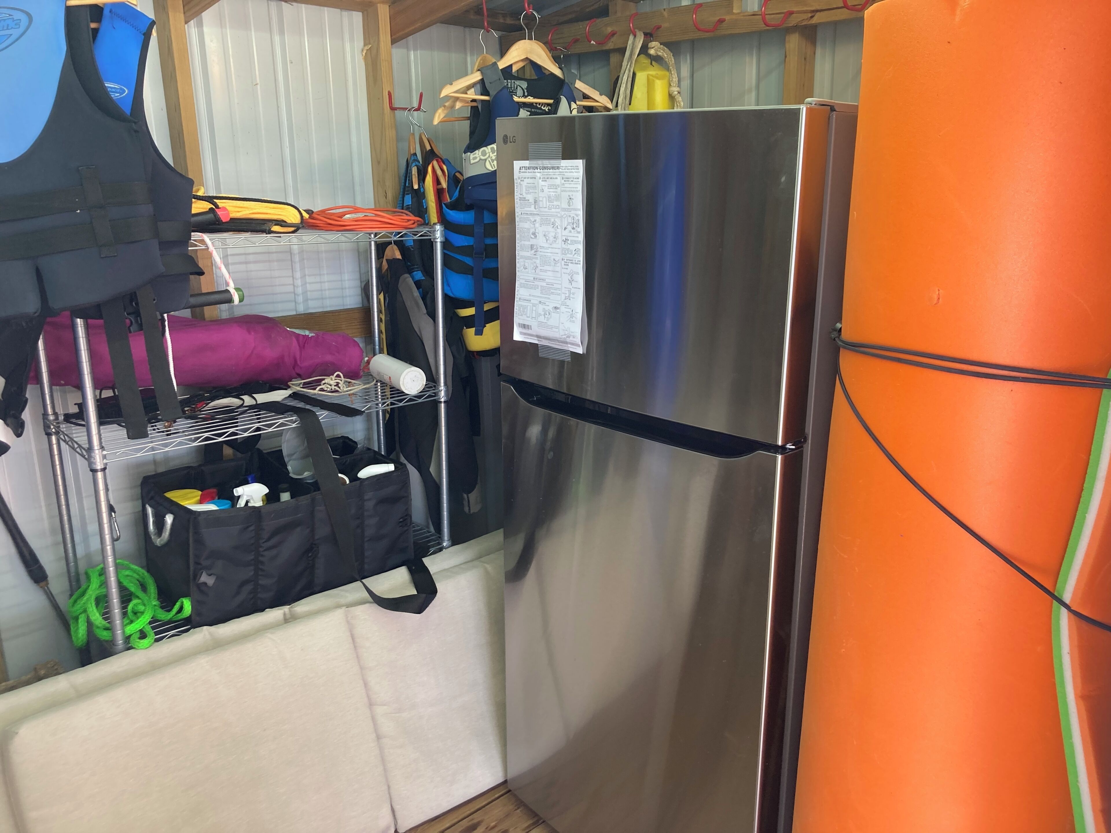 Una cocina compacta con un refrigerador de acero inoxidable, un estante de madera con diversos objetos, y una pequeña bolsa negra en el suelo.