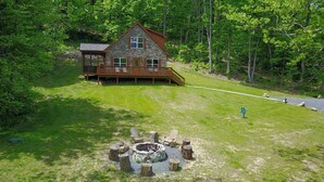 Une cabane en pierre dotée d’une terrasse, entourée d’une zone herbeuse et d’arbres.