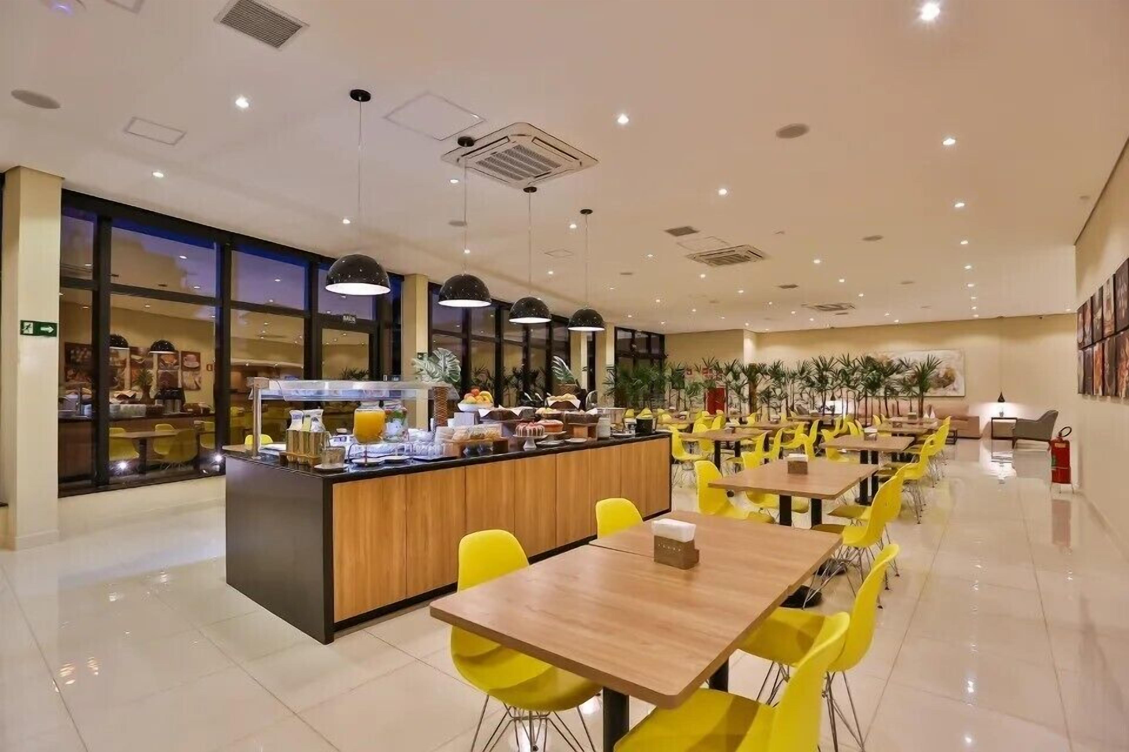 A modern restaurant with a central counter, yellow chairs, and tables.