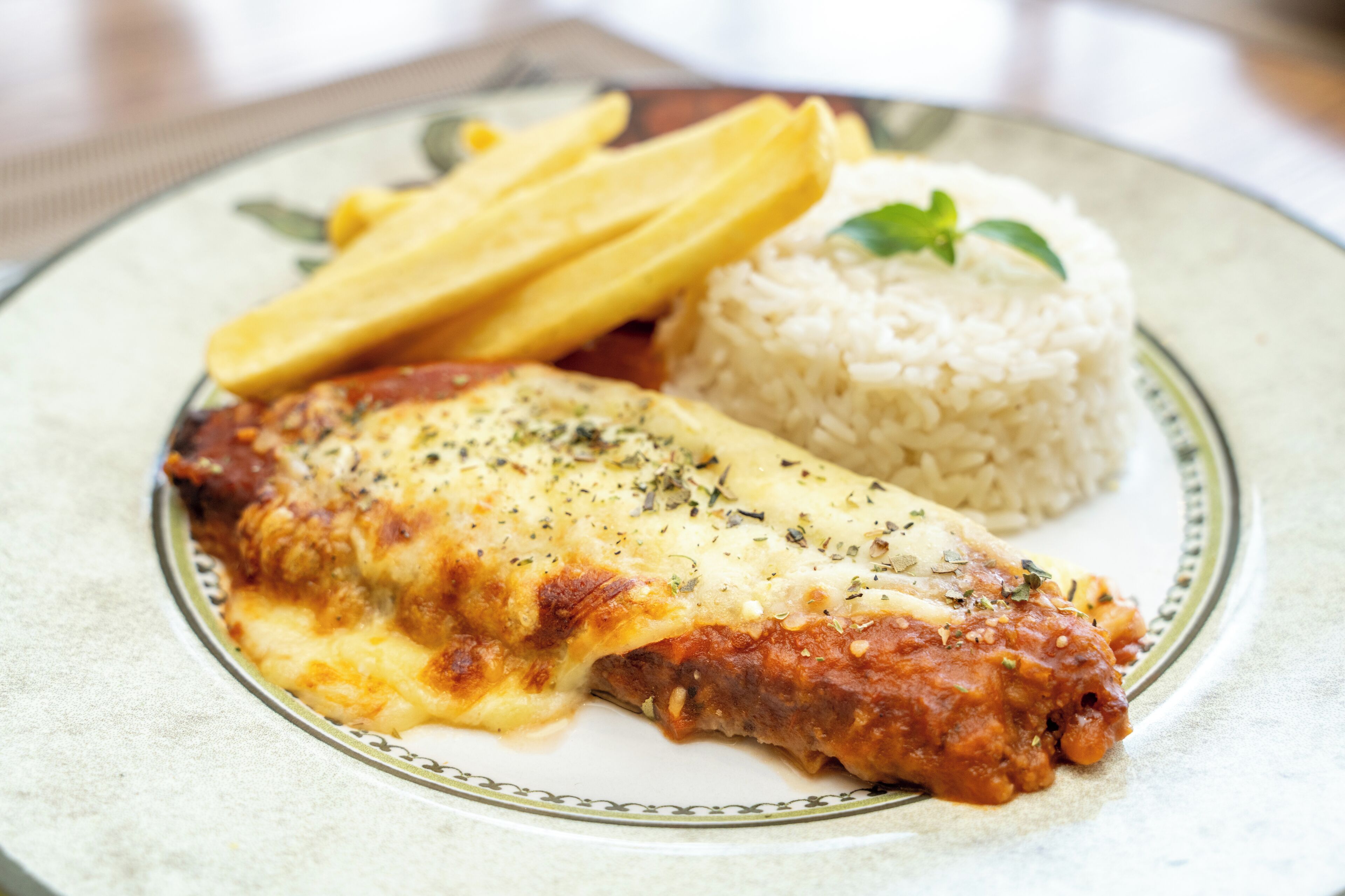 A plate with a chicken parmesan, rice, and French fries.