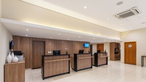 A hotel reception area with wooden reception desks, a flat-screen TV, and a digital display. - Blue Tree Jaguariuna (Jaguariuna)