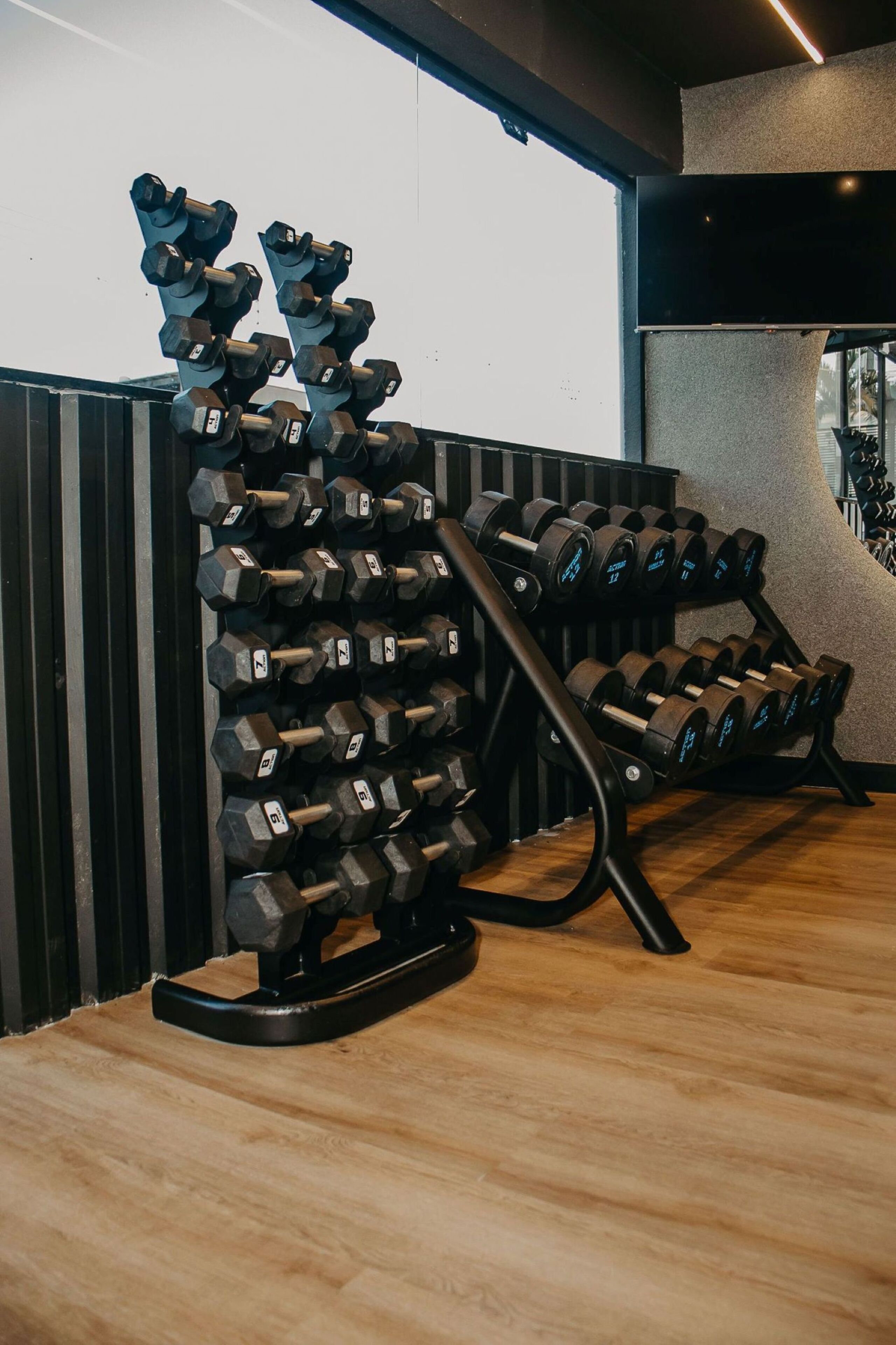 Un gimnasio con varios soportes para mancuernas y suelo de madera.