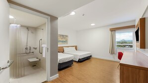 A hotel room with a shower, two beds, a small sink, a wooden desk, a red chair, and a window with a view. - Blue Tree Jaguariuna (Jaguariuna)