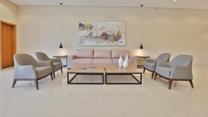 A modern living room with a beige sofa, two armchairs, and a coffee table. There is a painting on the wall and pendant lighting above the sofa. - Blue Tree Jaguariuna (Jaguariuna)