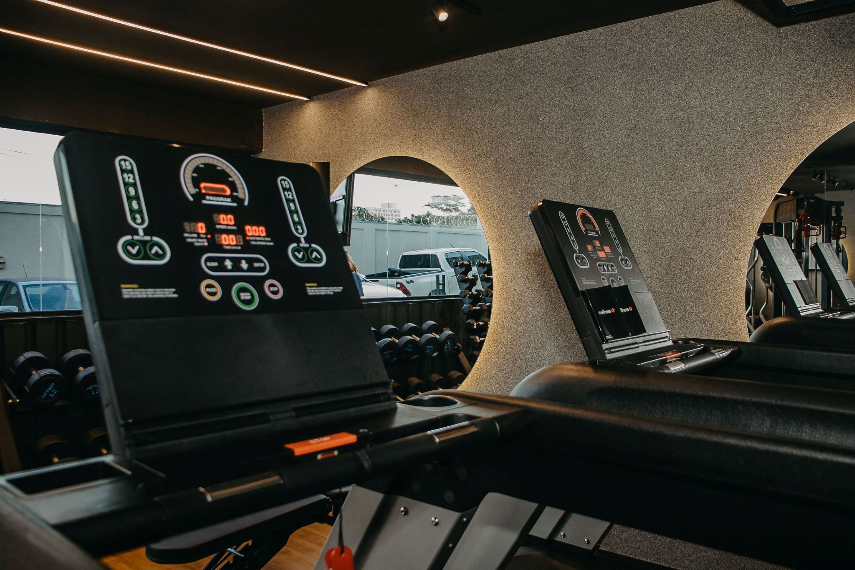 A gym with exercise equipment, a digital display, and a view of the outside.