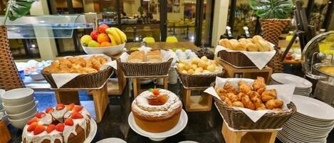 Un bufé con diversas opciones de repostería, como pasteles y bollos, dispuesto sobre una mesa con platos y utensilios para servir.