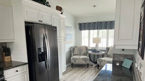 A kitchen with white cabinetry, a black refrigerator, a dining area with two chairs, a round table, and a window with curtains. - Gated Community/Lazy River/Pool/Tennis/Granite/Tile/Lanai with Kitchen (Naples)
