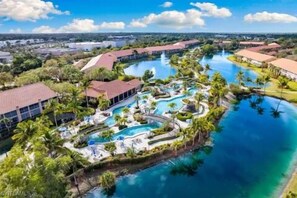 An aerial view of a resort with multiple swimming pools, palm trees, and a large body of water. - Gated Community/Lazy River/Pool/Tennis/Granite/Tile/Lanai with Kitchen (Naples)