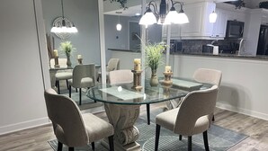 A dining area with a glass table surrounded by chairs, a patterned rug, and a kitchen in the background. - Gated Community/Lazy River/Pool/Tennis/Granite/Tile/Lanai with Kitchen (Naples)