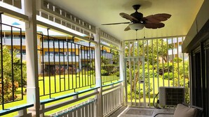 A covered outdoor area with a ceiling fan, a chair, and a view of a building with balconies.