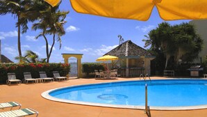 A swimming pool with lounge chairs and umbrellas, surrounded by palm trees and a gazebo.