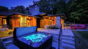 Una vasca idromassaggio di fronte a una casa in pietra con un patio in legno e mobili da esterno.