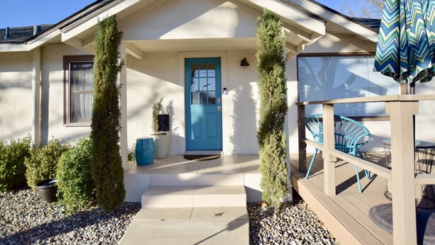 A house with a blue door, a covered porch with chairs, and a small garden with potted plants.
