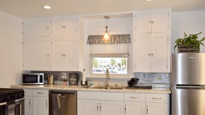 A modern kitchen with white cabinets, stainless steel appliances, and a window with blinds.