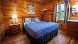A wooden cabin bedroom with a bed, nightstand, dresser, and a ceiling fan.