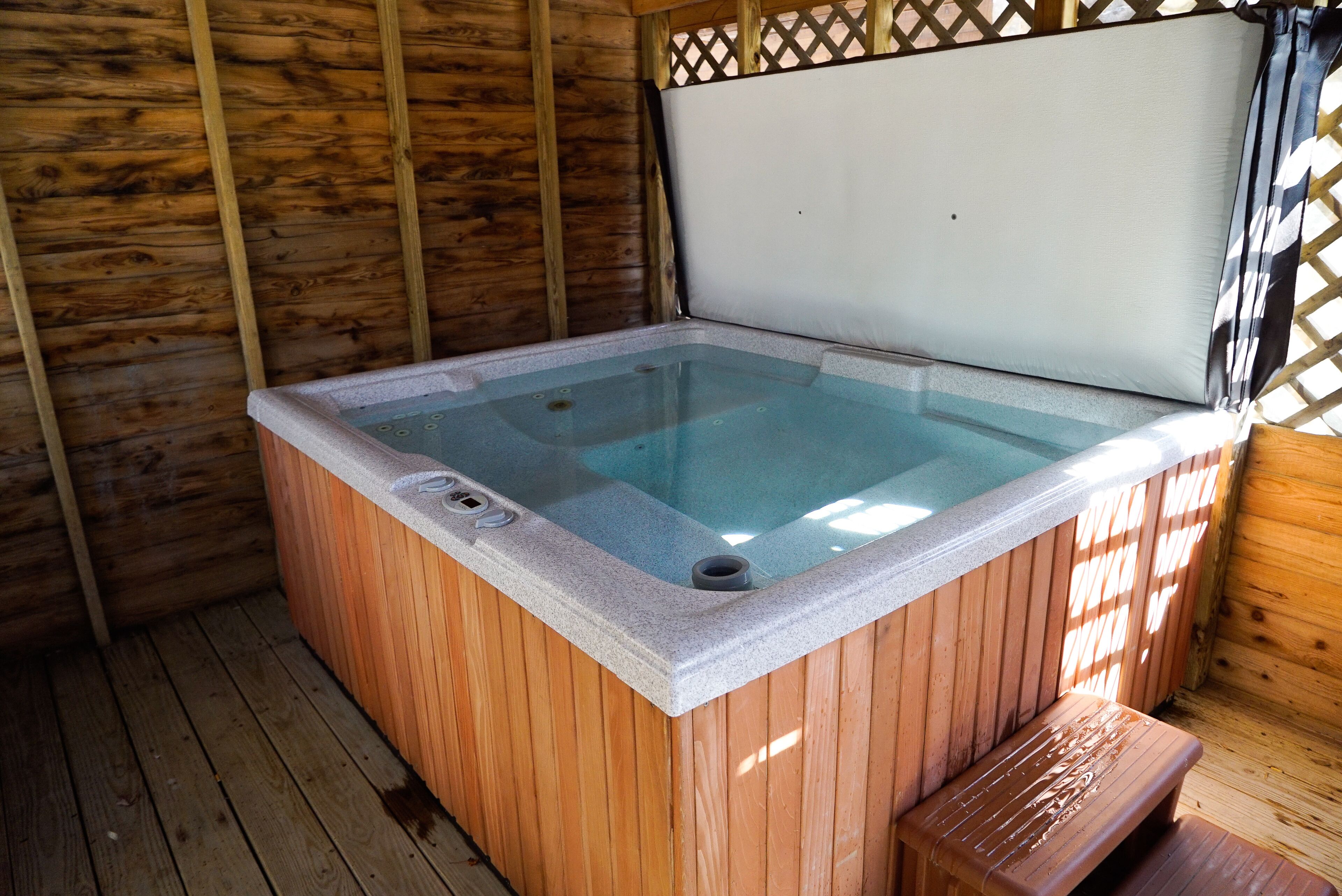 A hot tub with a wooden exterior and a white interior, surrounded by wooden walls and a wooden deck.