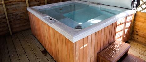 A hot tub with a wooden exterior and a white interior, surrounded by wooden walls and a wooden deck.