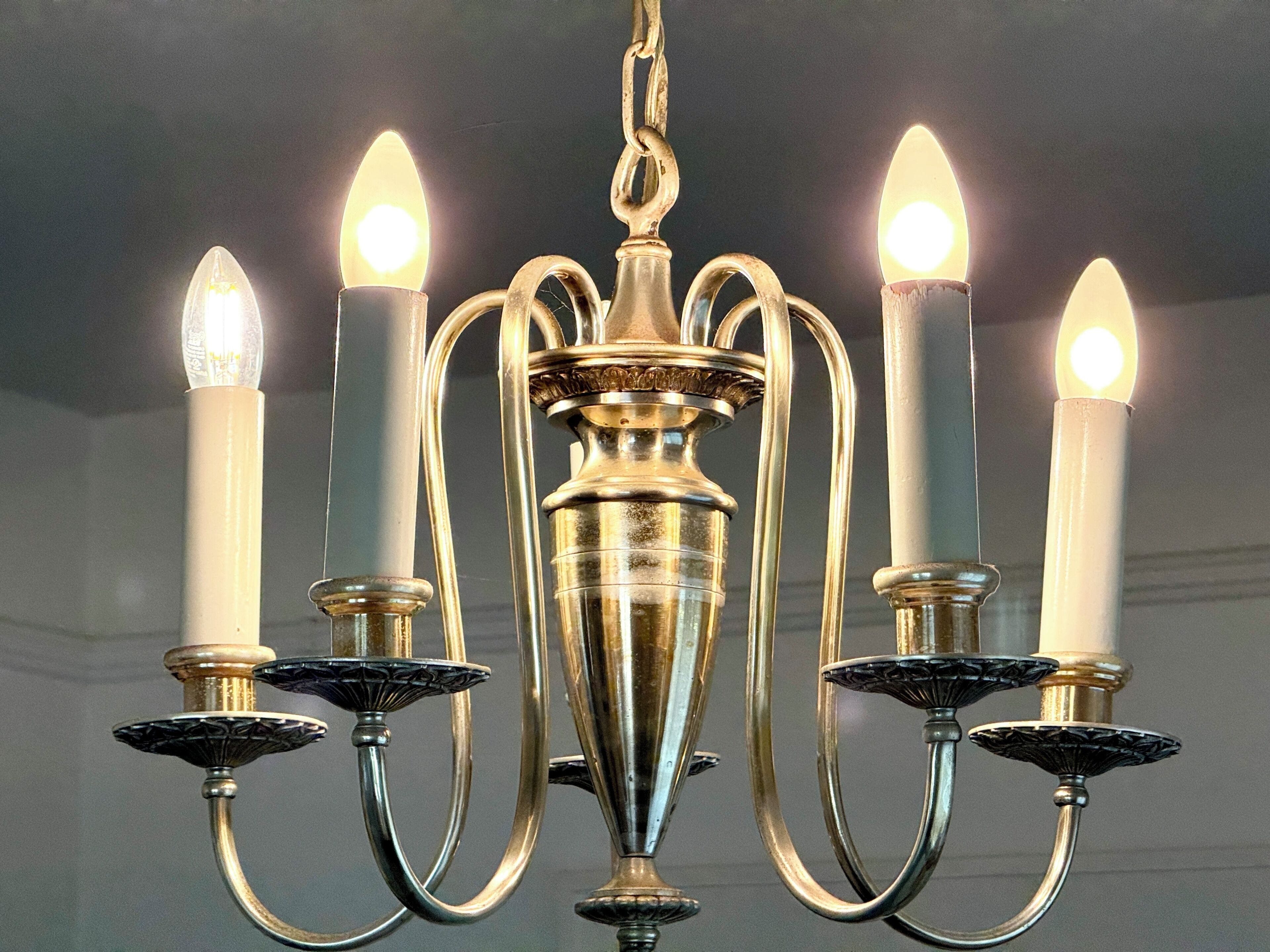 A chandelier with five candle-like lights, a central ornate metal fixture, and a chain.