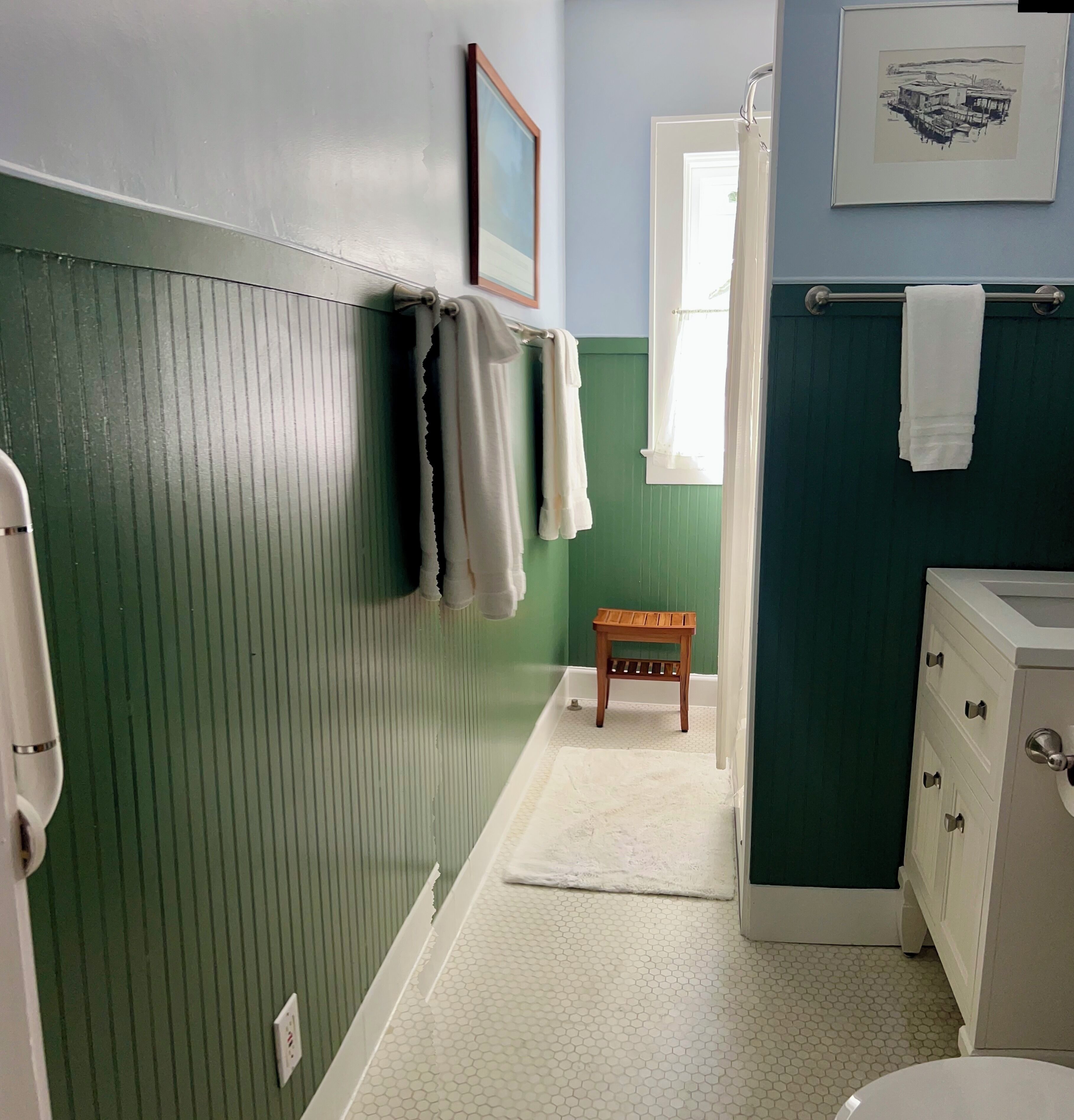 Une petite salle de bain aux murs verts et bleus, avec un tabouret en bois et un lavabo blanc.