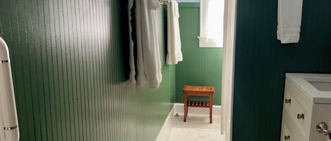 Une petite salle de bain aux murs verts et bleus, avec un tabouret en bois et un lavabo blanc.
