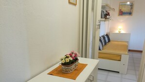 Un couloir avec une armoire blanche, une petite table ornée d’un arrangement floral et un lit recouvert d’une couverture jaune.