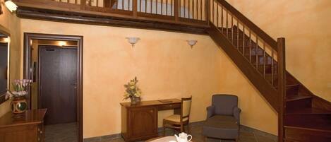 Una habitación acogedora con una escalera de madera, un escritorio con silla, una pequeña mesa con tetera y un sofá.